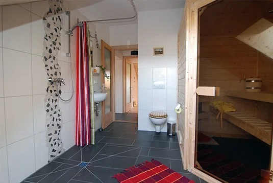 Das größere Bad mit Dusche, WC und offen stehender Saunatür aus Holz